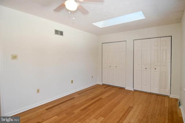 unfurnished bedroom with ceiling fan, light wood-type flooring, and multiple closets