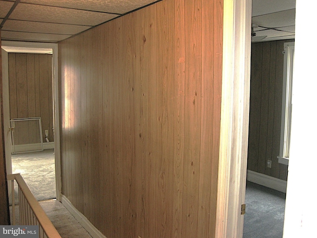 hallway with wood walls, carpet flooring, and a paneled ceiling