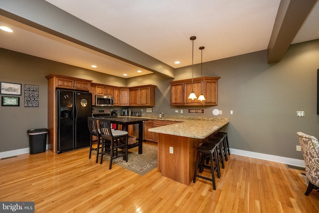 kitchen with pendant lighting, kitchen peninsula, black fridge with ice dispenser, a kitchen breakfast bar, and light wood-type flooring