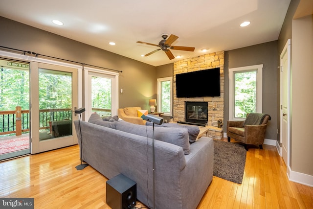 living room featuring ceiling fan, a stone fireplace, light hardwood / wood-style floors, and a wealth of natural light