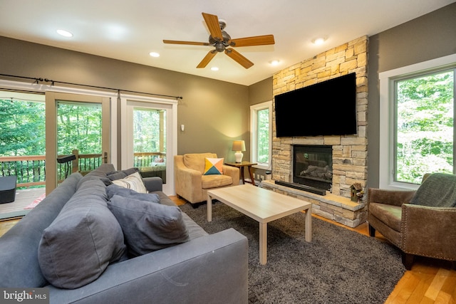 living room featuring wood-type flooring, ceiling fan, and a stone fireplace