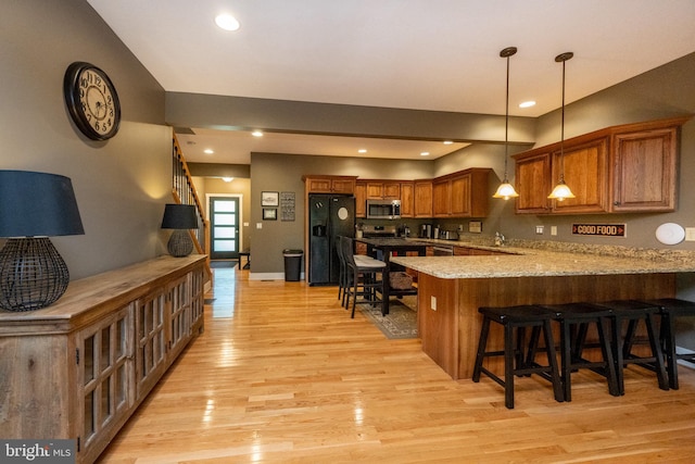 kitchen featuring pendant lighting, light hardwood / wood-style floors, kitchen peninsula, a kitchen breakfast bar, and black fridge with ice dispenser