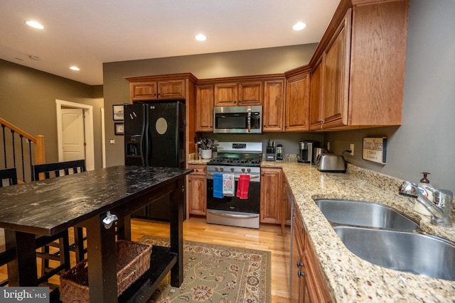 kitchen with light hardwood / wood-style flooring, light stone counters, appliances with stainless steel finishes, and sink