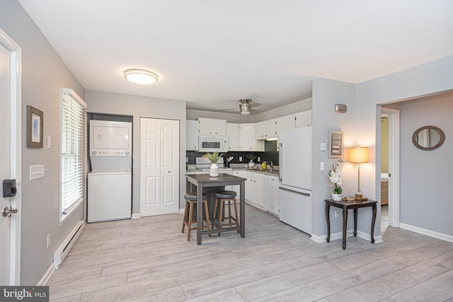 kitchen with white appliances, light hardwood / wood-style flooring, a baseboard radiator, and stacked washing maching and dryer