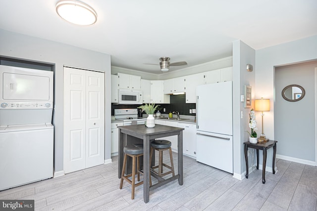 kitchen featuring light wood-type flooring, stacked washer / drying machine, white appliances, and white cabinets