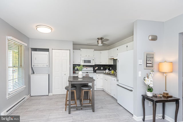 kitchen with stacked washing maching and dryer, a healthy amount of sunlight, baseboard heating, and white appliances