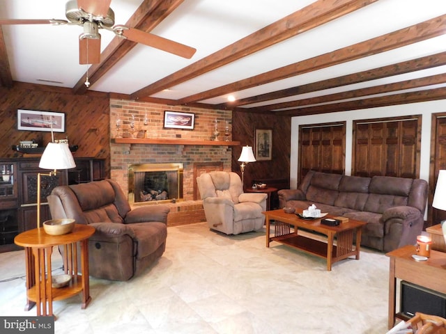 living room with a fireplace, wooden walls, ceiling fan, and beamed ceiling