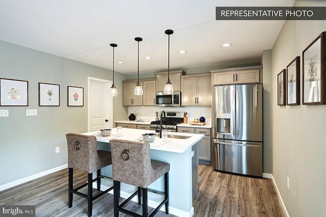 kitchen with dark wood-type flooring, a center island with sink, a breakfast bar area, pendant lighting, and appliances with stainless steel finishes