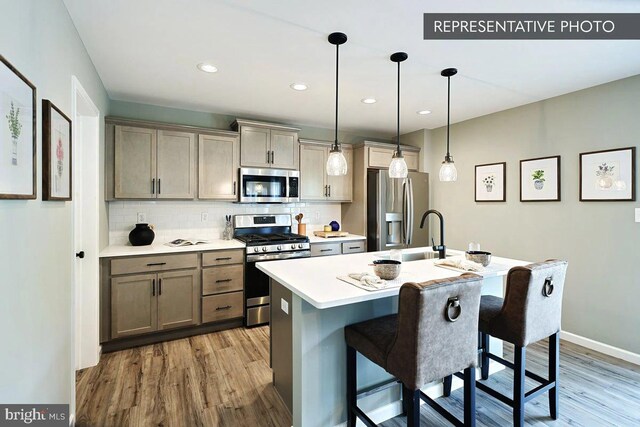 kitchen featuring light hardwood / wood-style floors, stainless steel appliances, hanging light fixtures, sink, and a kitchen island with sink