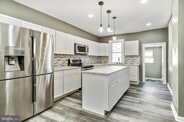 kitchen with pendant lighting, a kitchen island, appliances with stainless steel finishes, white cabinets, and light hardwood / wood-style floors