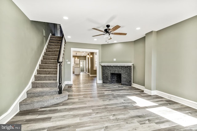 unfurnished living room with light wood-type flooring, ceiling fan, and a brick fireplace