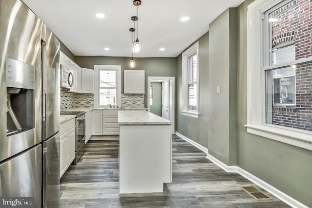 kitchen with light stone countertops, hanging light fixtures, stainless steel appliances, a center island, and white cabinetry