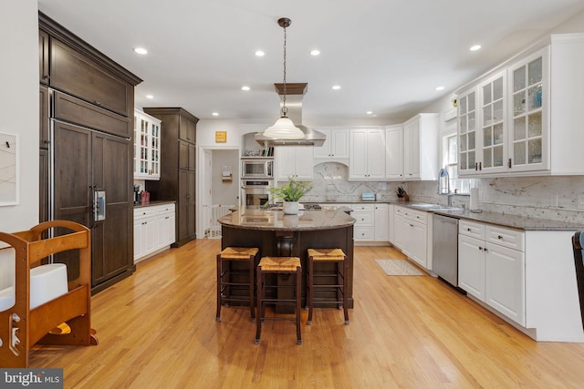 kitchen with a center island, built in appliances, light wood-type flooring, and light stone countertops