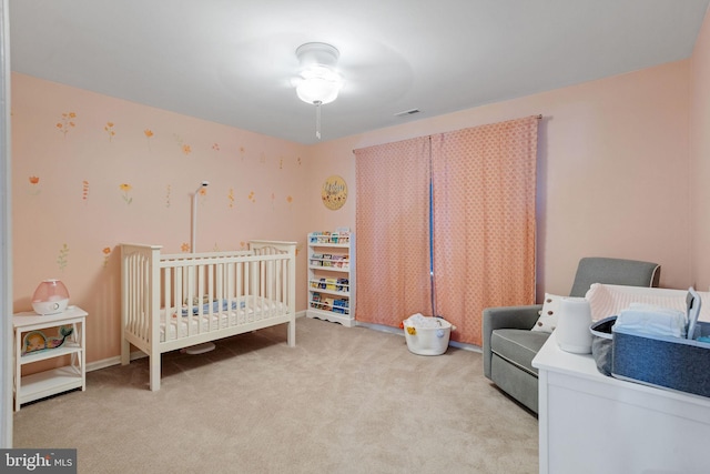 carpeted bedroom featuring ceiling fan and a crib