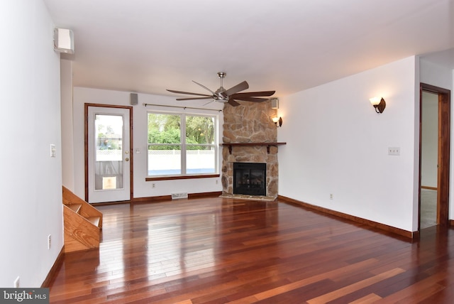 unfurnished living room featuring ceiling fan, a stone fireplace, and dark wood-type flooring