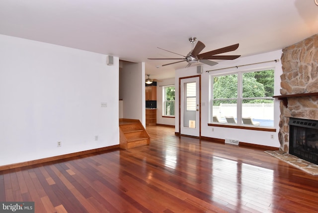 unfurnished living room with wood-type flooring, ceiling fan, and a stone fireplace