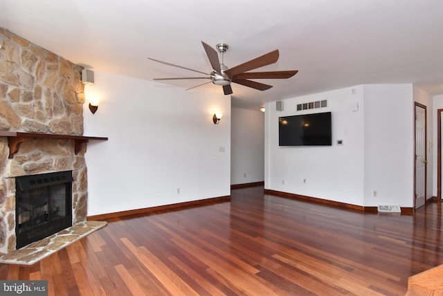 unfurnished living room featuring a stone fireplace, dark wood-type flooring, and ceiling fan