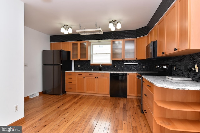 kitchen with backsplash, light stone countertops, light wood-type flooring, black appliances, and sink