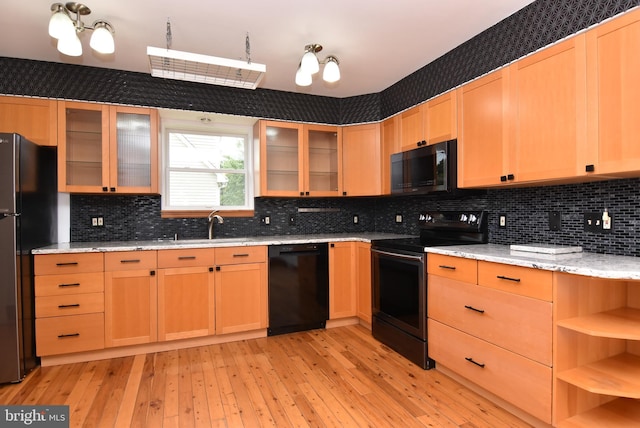 kitchen featuring light stone counters, tasteful backsplash, black appliances, an inviting chandelier, and light hardwood / wood-style floors