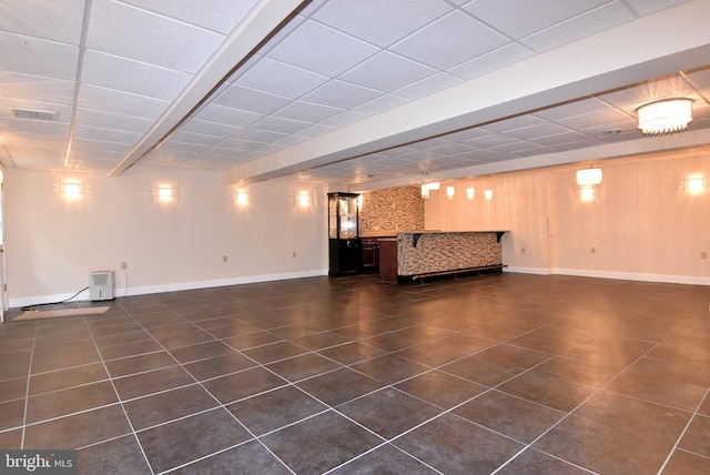 basement with a paneled ceiling and dark tile patterned flooring