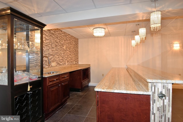 bar with hanging light fixtures, light stone counters, dark tile patterned floors, a paneled ceiling, and sink