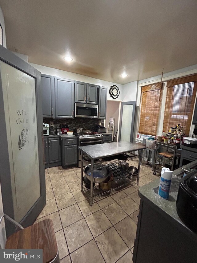 kitchen with gray cabinetry, light tile patterned floors, tasteful backsplash, and range