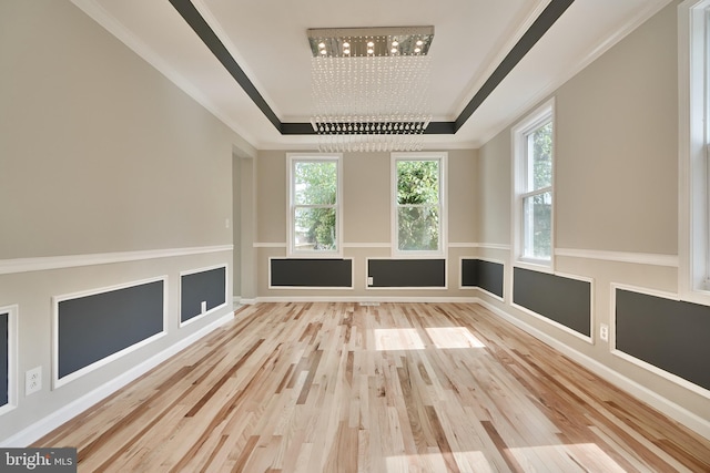 empty room featuring wood-type flooring, an inviting chandelier, a raised ceiling, and crown molding