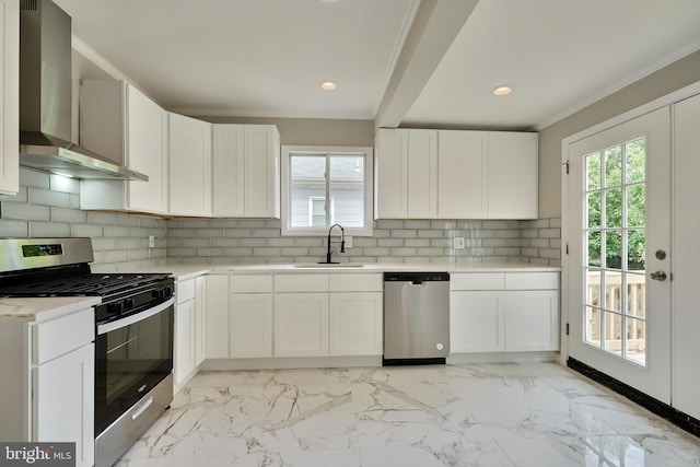 kitchen featuring tasteful backsplash, white cabinets, wall chimney range hood, and appliances with stainless steel finishes