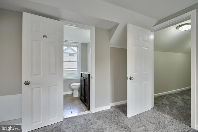 unfurnished bedroom with ensuite bath, carpet floors, and lofted ceiling