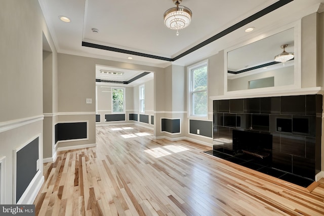 unfurnished living room featuring a raised ceiling, a tiled fireplace, hardwood / wood-style flooring, and ornamental molding