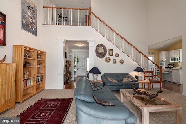 carpeted living room with ornamental molding, a high ceiling, and decorative columns