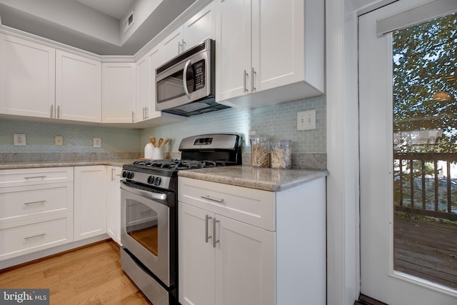 kitchen with light stone counters, tasteful backsplash, white cabinetry, stainless steel appliances, and light wood-type flooring