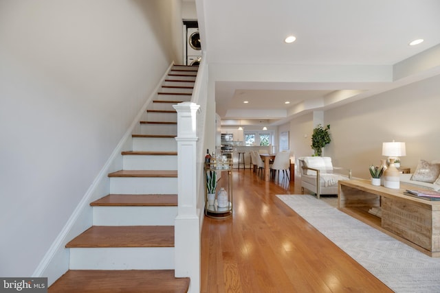 stairway featuring a tray ceiling, hardwood / wood-style flooring, and stacked washing maching and dryer