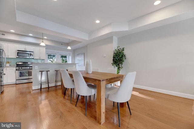 dining room with light hardwood / wood-style floors and a tray ceiling