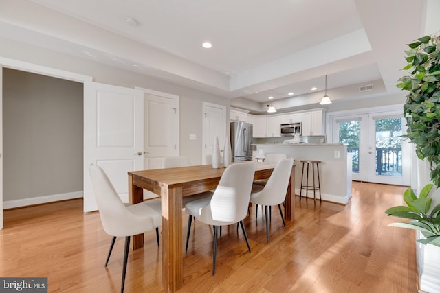 dining room with french doors, a raised ceiling, and light hardwood / wood-style floors