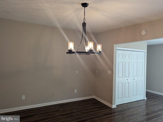 unfurnished dining area with dark wood-type flooring, a textured ceiling, and a chandelier