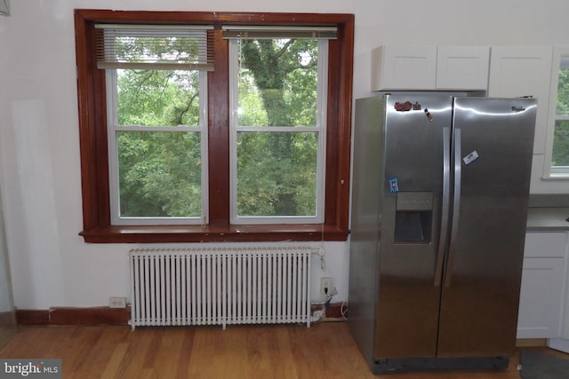 kitchen with radiator, light wood-type flooring, stainless steel fridge, and white cabinetry