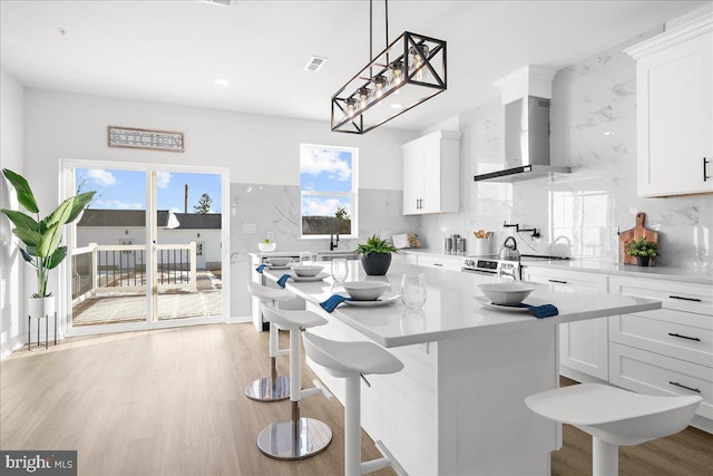 kitchen featuring a kitchen breakfast bar, white cabinetry, and wall chimney range hood