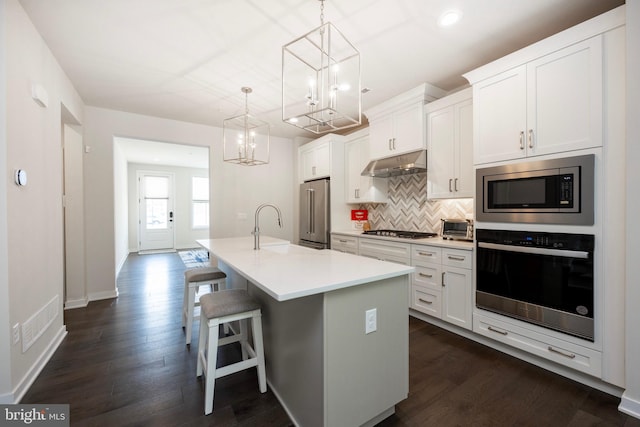 kitchen with appliances with stainless steel finishes, sink, a center island with sink, white cabinetry, and hanging light fixtures