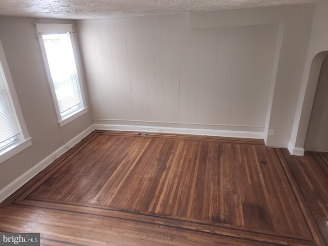 empty room with a textured ceiling, dark hardwood / wood-style floors, and wooden walls