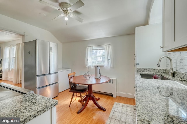 kitchen featuring light stone countertops, stainless steel fridge, light hardwood / wood-style floors, sink, and radiator heating unit