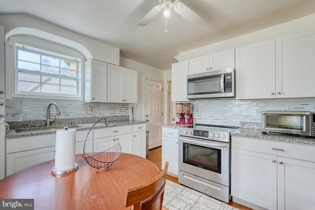 kitchen with light stone counters, stainless steel appliances, white cabinetry, ceiling fan, and tasteful backsplash