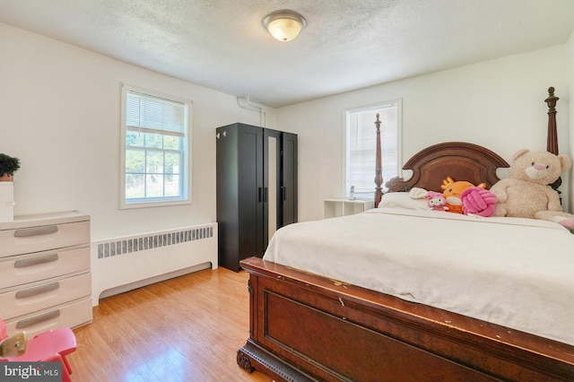 bedroom with radiator heating unit, a textured ceiling, and light hardwood / wood-style flooring