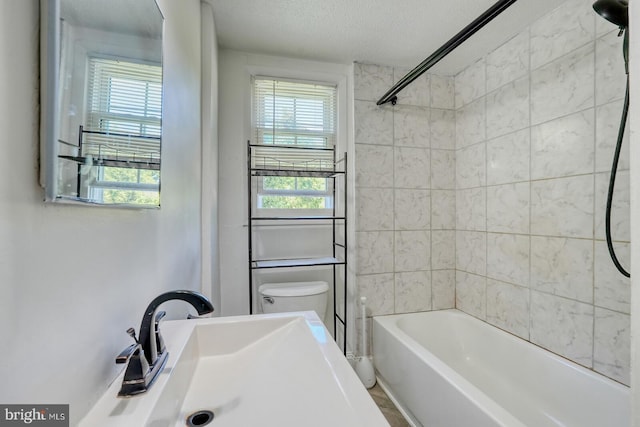 full bathroom with tiled shower / bath combo, toilet, sink, and a textured ceiling