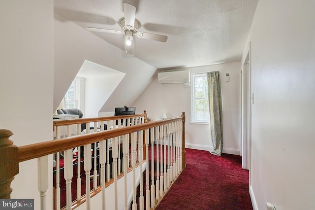 corridor with a textured ceiling, vaulted ceiling, an AC wall unit, and carpet floors