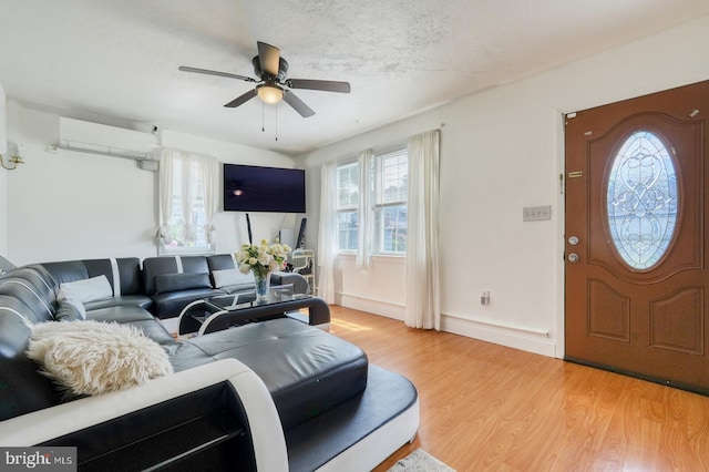 living room with a textured ceiling, a wall mounted AC, ceiling fan, and wood-type flooring