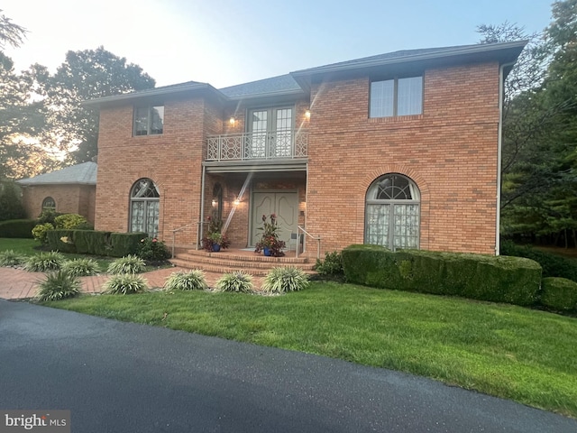 view of front of property with a balcony, a yard, and french doors