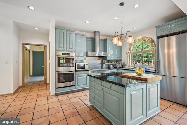 kitchen with wall chimney exhaust hood, a kitchen island, light tile patterned floors, pendant lighting, and stainless steel appliances