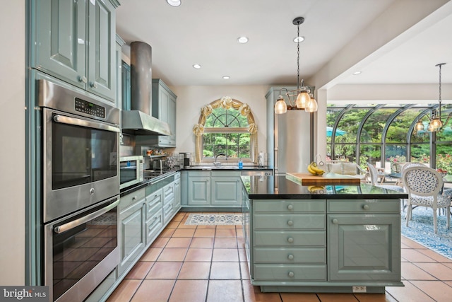 kitchen with an inviting chandelier, light tile patterned floors, double oven, and wall chimney range hood