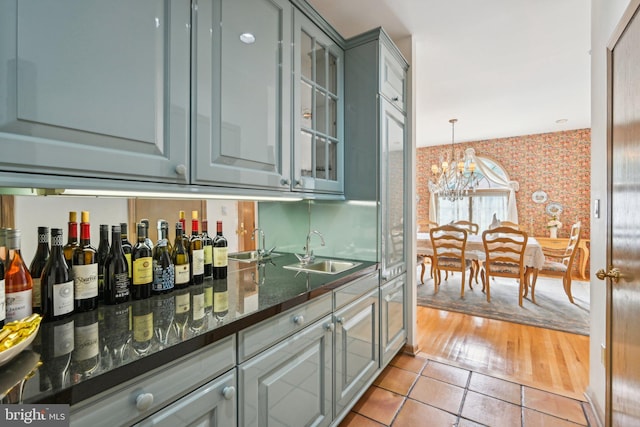 bar featuring dark stone counters, light wood-type flooring, a chandelier, sink, and gray cabinetry